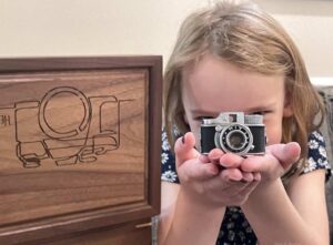 Young girl holding vintage toy camera in front of keepsake box engraving