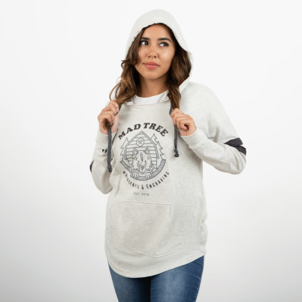 Woman wearing a light gray Mad Tree Woodcrafts & Engraving hoodie with the hood up, holding the drawstrings and looking to the side with a soft smile.