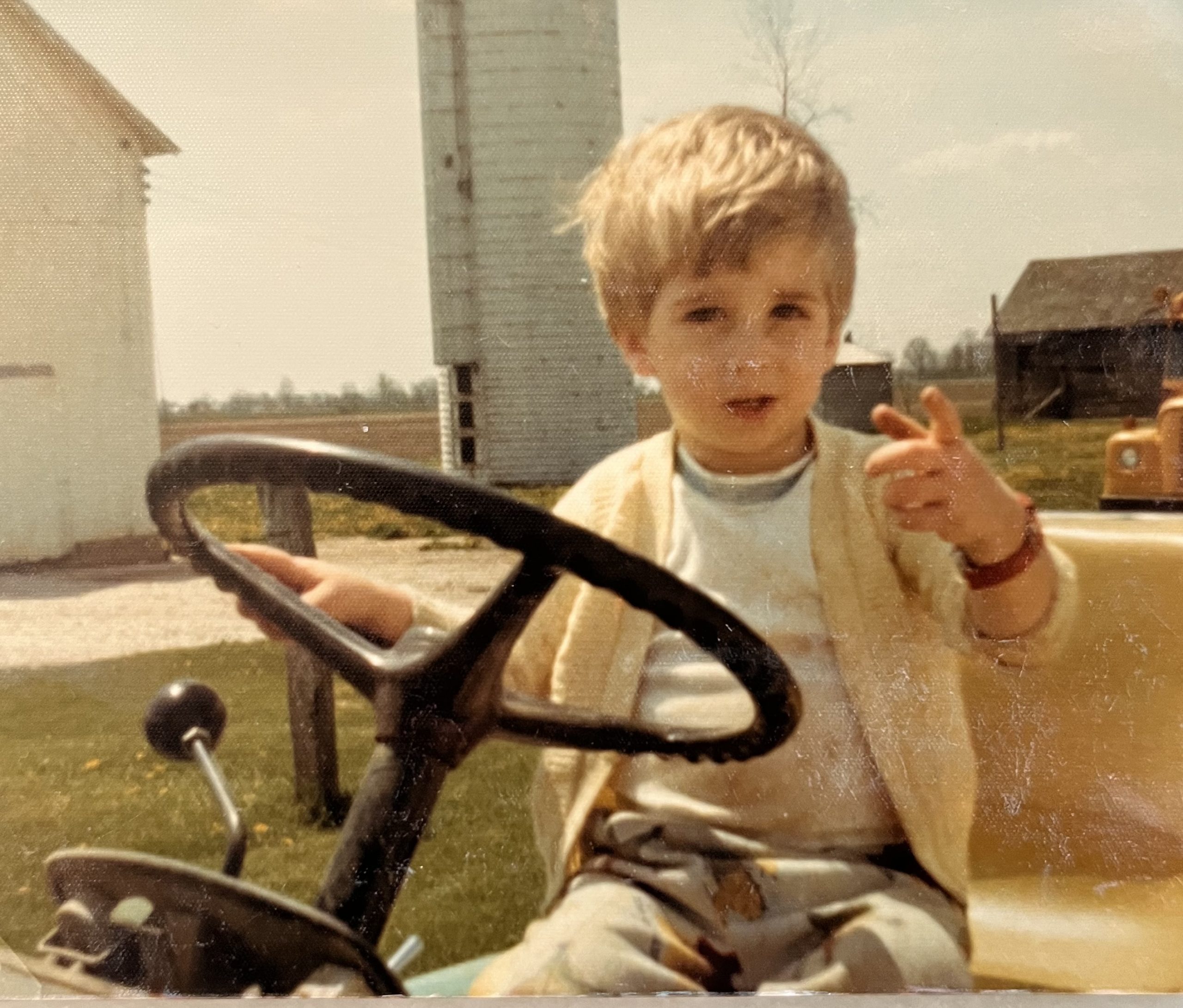 Childhood photo of Tyler Bishop Hall sitting on his grandfather’s farm tractor.