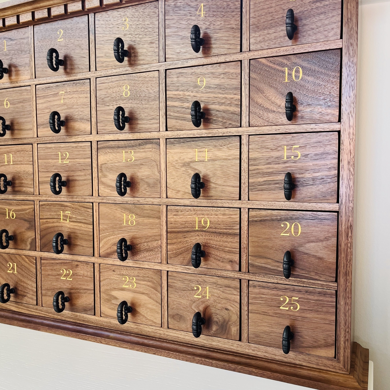 Angled view of a handcrafted walnut advent calendar showing numbered drawers and antique-style drawer pulls