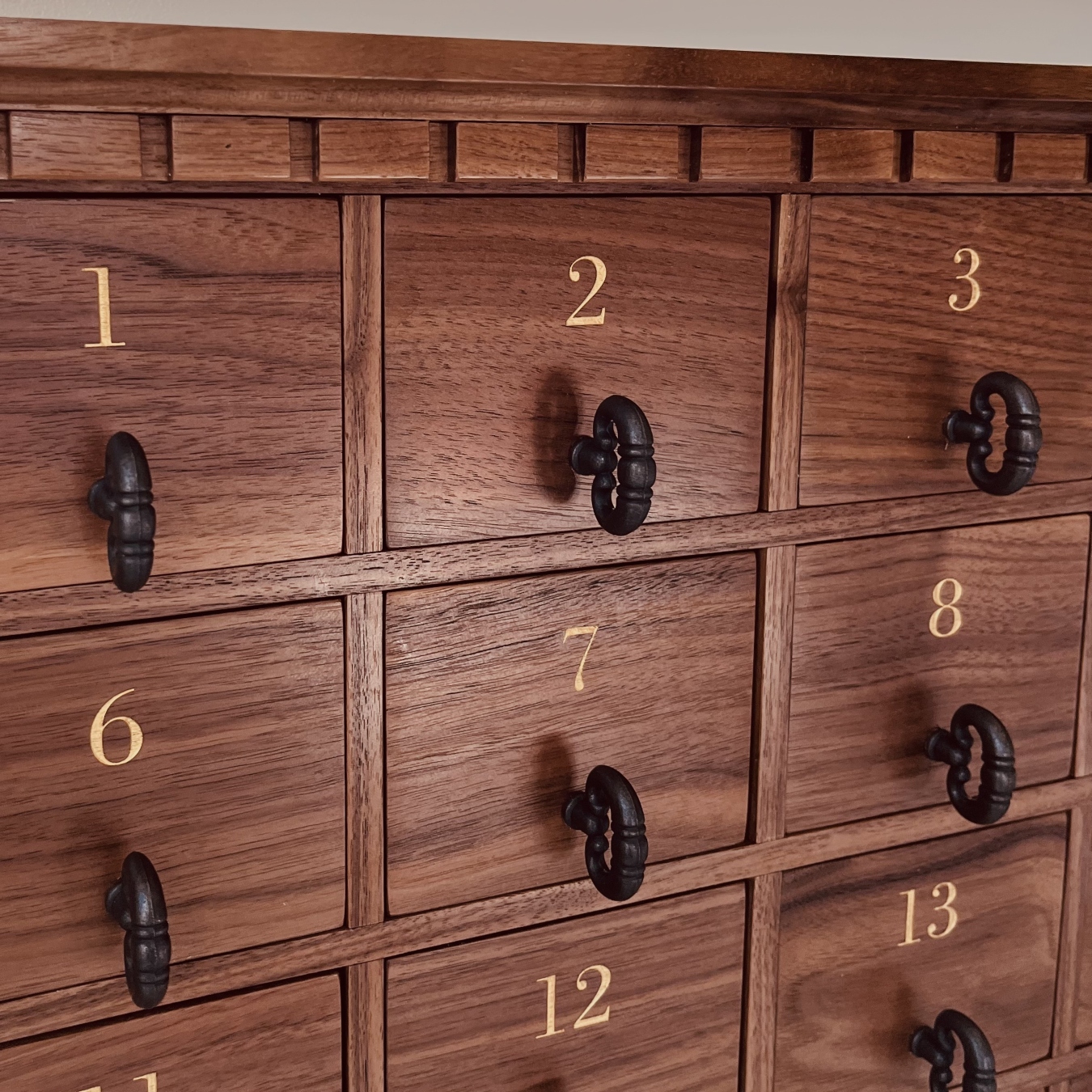 Close-up of numbered walnut drawers with antique-style pulls on a handcrafted advent calendar